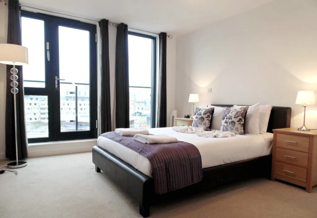 Bright bedroom with large windows, white walls, and contemporary furnishings.
