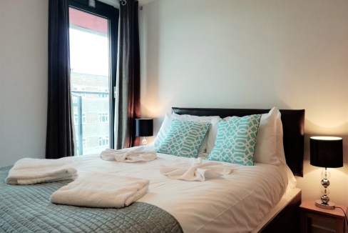 Bright bedroom with large window, contemporary bedding, and elegant lighting.