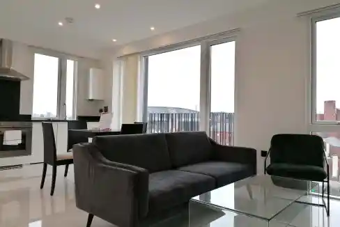 Spacious living area featuring a black sofa, glass coffee table, and ample natural light from large.