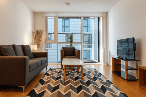 Spacious living room featuring a sofa, armchair, and flat-screen TV with city views.