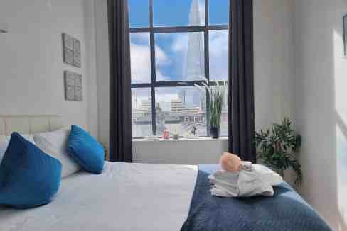 Interior view of a modern bedroom with a large window overlooking The Shard in London.
