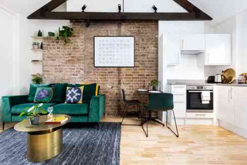 Bright living space featuring a cozy green sofa, stylish coffee table, and minimalist kitchen with w.