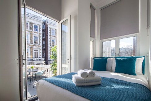 Bright bedroom in Kensington serviced apartment with balcony and city views.