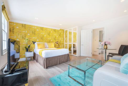 Bright hotel suite with yellow accent wall featuring swan and floral wallpaper, modern furnishings,.
