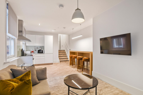Comfortable living area with sofa, cushions, and wall-mounted TV in a contemporary serviced apartmen.