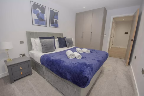 Edgware Road Serviced Apartments modern bedroom with wooden floors, neutral colours, and purple soft furnishings and wall art.