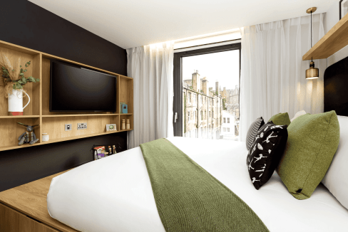 Modern hotel room with a large bed, green accents, and city views near Grassmarket Square.