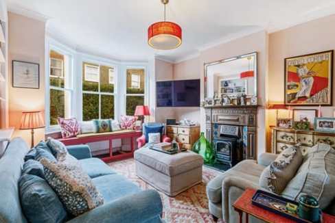 Cozy living room with large bay windows, colorful cushions, and vintage decor in a charming Chiswick.