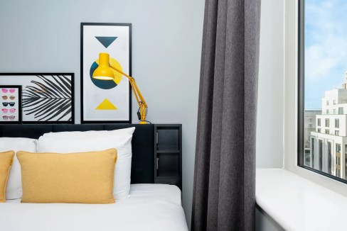 Contemporary hotel room featuring colorful artwork, yellow lamp, and large window overlooking Liverp.