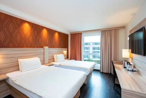 Modern hotel room with two beds, stylish decor, and a large window at Heidelberg Kirchheim Aparthote.