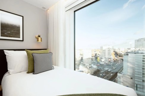 Bright hotel room with large window overlooking London skyline at Paddington Basin.