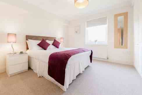 Bedroom with white walls, large window, and cozy bed with purple accents.