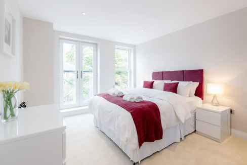 Bright bedroom in Reigate train station apartments with large windows and contemporary decor.