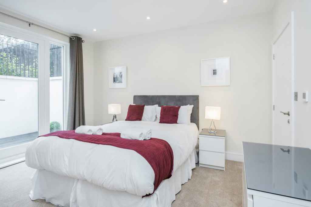 Bright bedroom in Surbiton Oak Hill Apartments with white walls and red bedding.