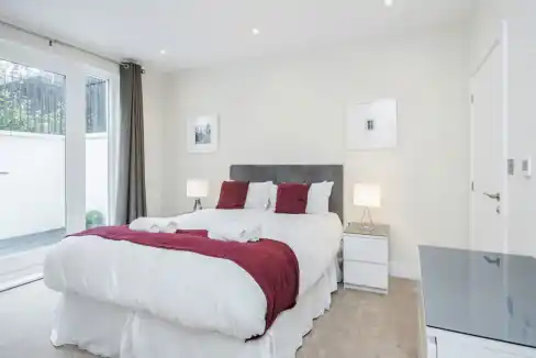 Bright bedroom in Surbiton Oak Hill Apartments with white walls and red bedding.