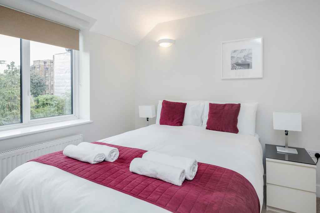 Bright, cozy bedroom in Surbiton Maple Road Apartments with white walls and red accents.