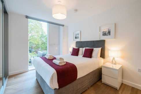 Apartment bedroom with large window, cozy bedding, and contemporary furnishings.