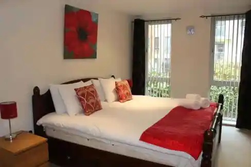 Comfortable bedroom with a large bed, decorative pillows, and natural light from balcony windows.