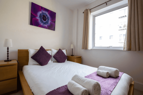 Bright bedroom with a large window and modern decor at Guildford Station View Apartments.