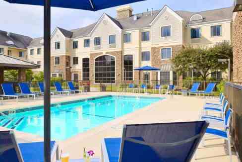 Outdoor pool at Boston Burlington Aparthotel with lounge chairs and umbrellas for relaxation.