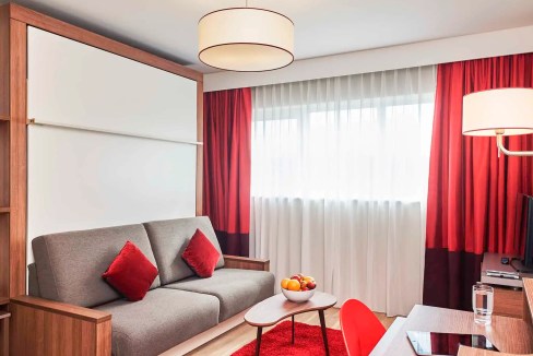Modern living room in Birmingham Digbeth Aparthotel with red accents and natural light.