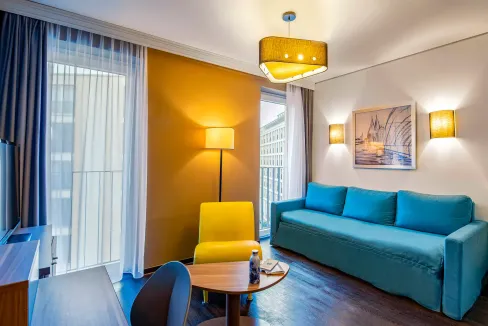 Bright hotel living room featuring a blue sofa, yellow armchair, and stylish decor in Cologne.