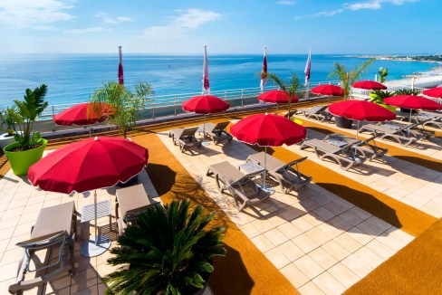 Relaxing seaside view with red umbrellas and sunbeds overlooking the Mediterranean.