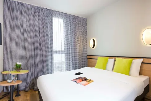 Bright hotel room with large window, stylish furnishings, and vibrant accent pillows.