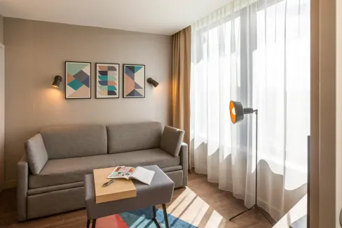 Modern Stratford International Aparthotel living room with sofa and large window, bright natural lig.