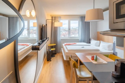 Aparthotel room in Freiburg North with modern furnishings and large windows offering city views.