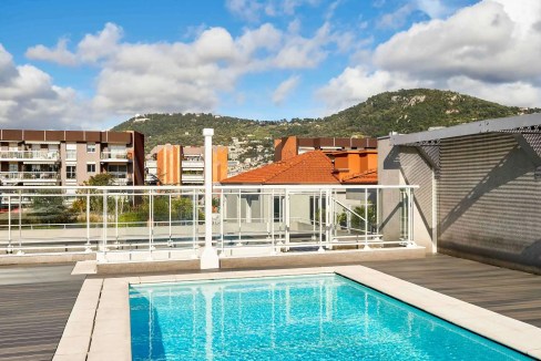 Rooftop swimming pool at Nice Riquier Aparthotel with city views and mountain backdrop.