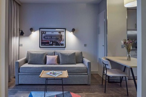 Heidelberg train station aparthotel living room with sofa, wall art, and dining table for guests.