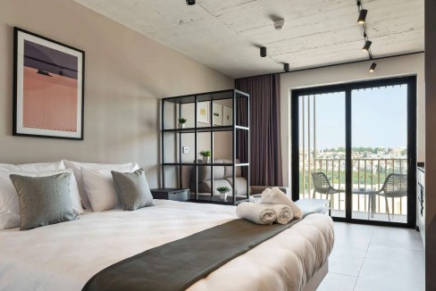 Spacious hotel room featuring a balcony with city views, stylish decor, and comfortable bedding at M.