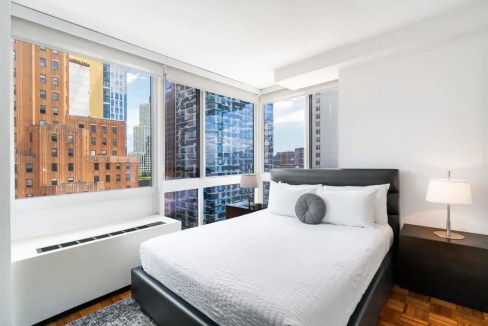 Bright bedroom in New York Jay St Apartments with large windows and city skyline view.