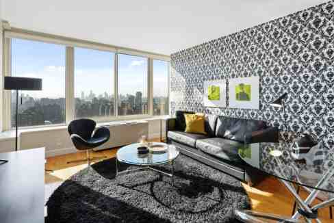 Stylish living room with large windows offering city views, black sofa, patterned accent wall, and c.