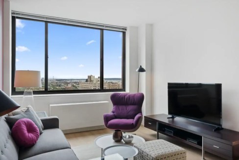 Modern living room with large window view of Brooklyn skyline.