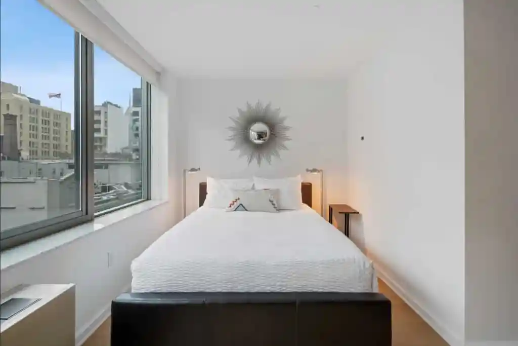 Bright, minimalist bedroom with large windows and city views at The High Line Galleries Apartments.