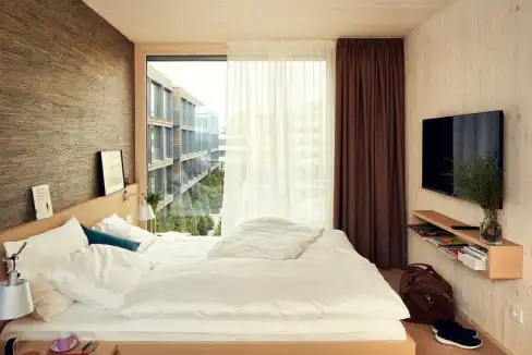 Aparthotel room in Munich Garching featuring a spacious bed, large window, and modern furnishings fo.