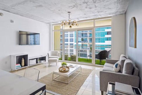 Living area with industrial ceilings and balcony access at Miami Wynwood luxury apartment