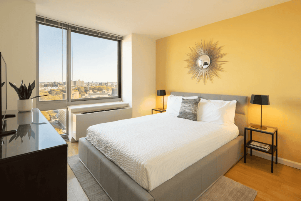 Bright bedroom in Brooklyn apartment with large window and city skyline view.