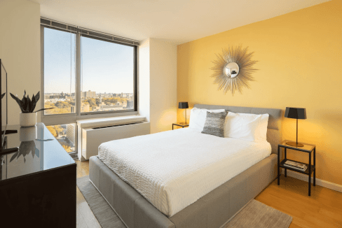 Bright bedroom in Brooklyn apartment with large window and city skyline view.