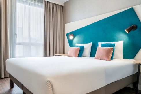 Modern hotel room with stylish decor at Paris Suresnes Seine Aparthotel, featuring a comfortable bed.