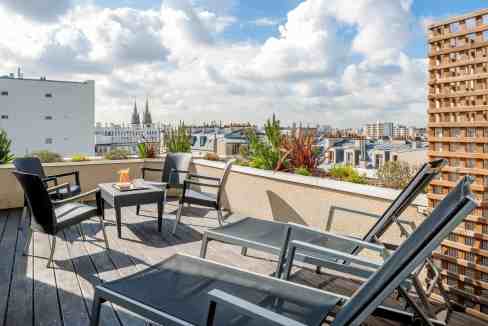 Rooftop terrace with lounge chairs and seating area overlooking Paris skyline at Parmentier Aparthot.