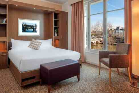 Hotel room with comfortable bed and scenic city view at Paris Pont Neuf Aparthotel.