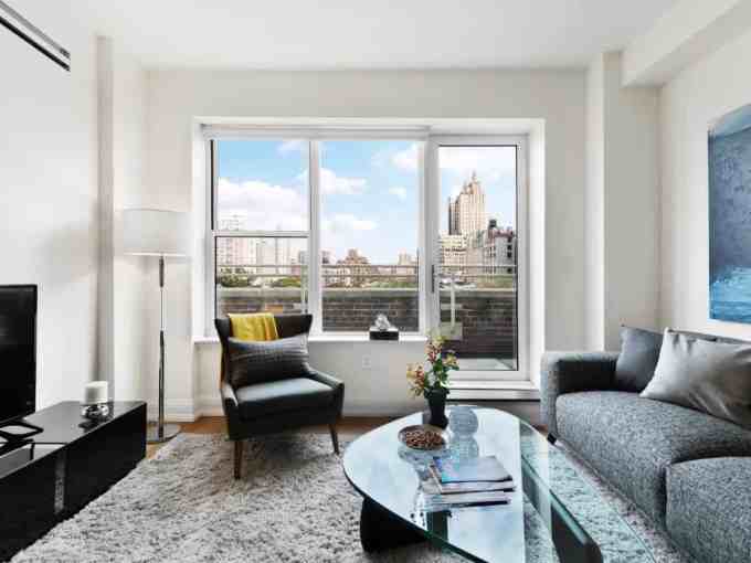 Bright living room in Central Park Apartments with large windows and city skyline backdrop.