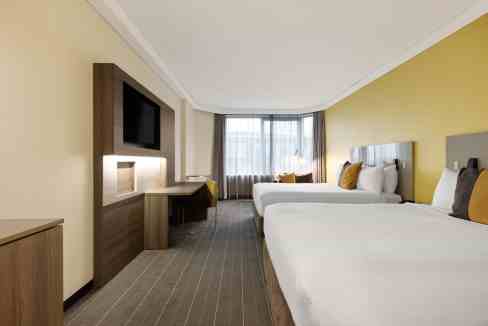 Modern Sydney hotel room with two beds, flat-screen TV, and large window.