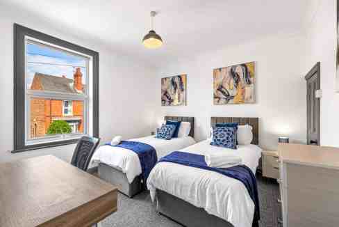 Bright bedroom with two beds, large window, and contemporary decor at Lincoln Riverside Apartments.