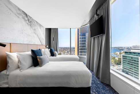 Comfortable hotel room with large windows overlooking North Sydney skyline and harbor.