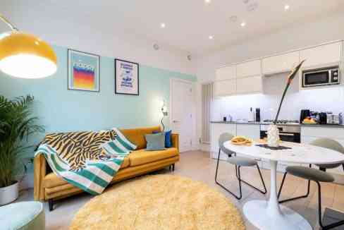 Living room with modern decor at Covent Garden Opera Apartments, featuring a mustard sofa, colorful.