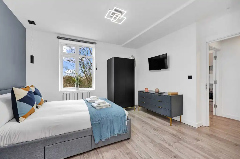 Bright, contemporary bedroom featuring a large window, minimalist furniture, and cozy bedding.